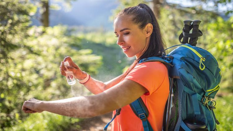 A woman applies bug spray to her hands to prevent bug bites during hike.